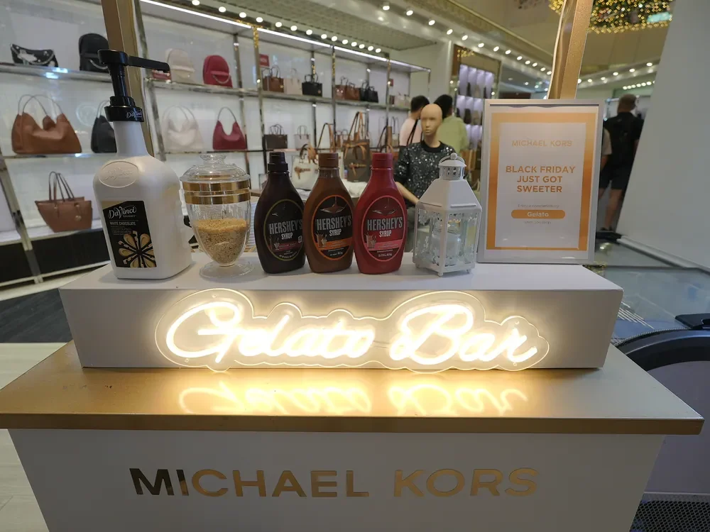 Michael Kors gelato-bar counter with toppings and an illuminated sign